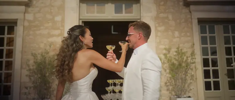 Les mariés trinquent au champagne devant la façade en pierre du Château de Saint-Bernard
