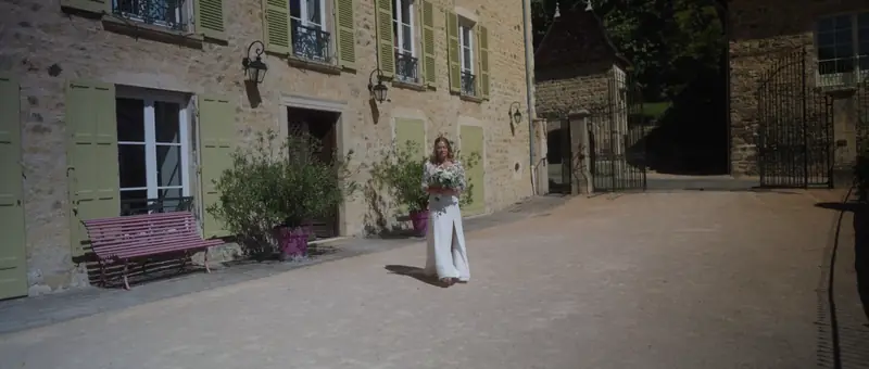 La mariée traverse la cour du Domaine de Vavril, devant la façade en pierre aux volets verts