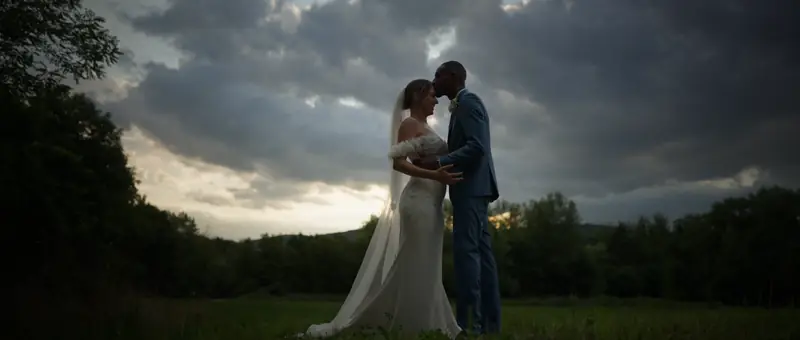 Les mariés enlacés dans une prairie, sous un ciel d'orage en fin de journée