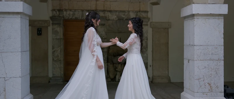 Les deux mariées main dans la main devant une porte du cloître de la Chartreuse de Pomier