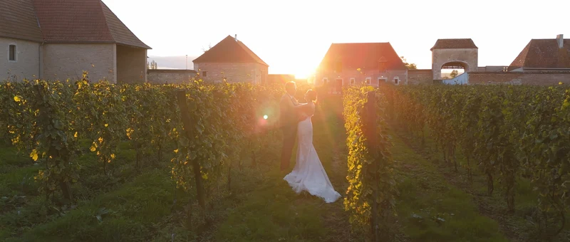 Les mariés enlacés dans les vignes du domaine au coucher du soleil, devant les bâtiments de l'abbaye