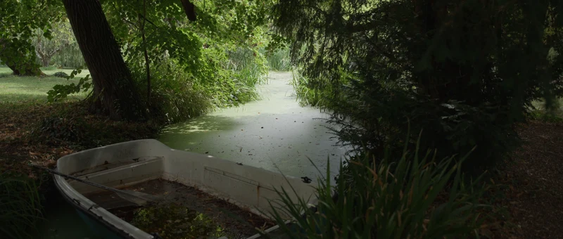 L'étang du Domaine de Blacons sous les arbres, avec une barque au bord de l'eau