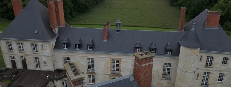 Les toits d'ardoise et les hautes cheminées de brique du Château de Thugny, vus du drone