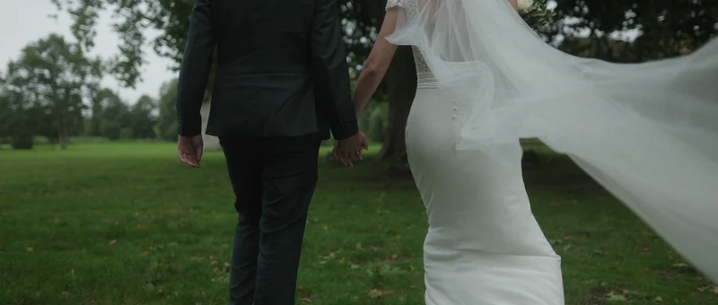 Les mariés de dos, main dans la main dans le parc du Château du Vivier, le voile au vent
