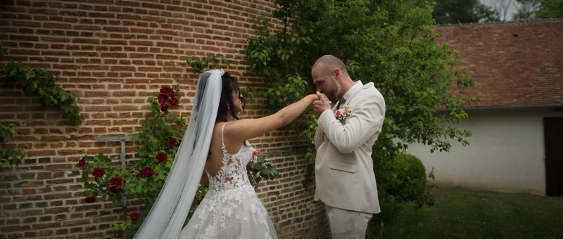 Le marié baise la main de la mariée contre le mur du colombier du Domaine du Colombier