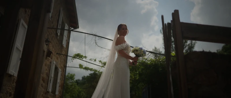 La façade en pierre et les volets blancs du gîte Au Champ Bonheur, avec la mariée sur la terrasse sous un ciel d'orage