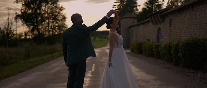 Les mariés dansent sur le chemin, le long du mur en pierre et de la tour ronde du Domaine de la Diligence, au coucher du soleil
