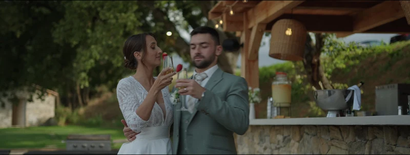 Les mariés trinquent devant le bar extérieur en pierre et la pergola en bois du Domaine de Noé