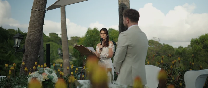 La mariée lit ses vœux au marié sous la voile d'ombrage de la terrasse des Pins Penchés, entre les palmiers