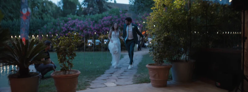 Les mariés traversent le jardin du Mas des Comtes de Provence le soir, entre les bougainvilliers et les guirlandes