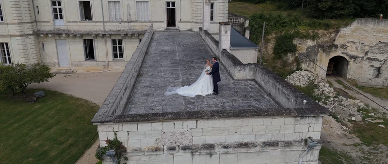 Les mariés sur la terrasse en pierre du Château de la Barbelinière, vus du drone, à côté d'une cave creusée dans la roche