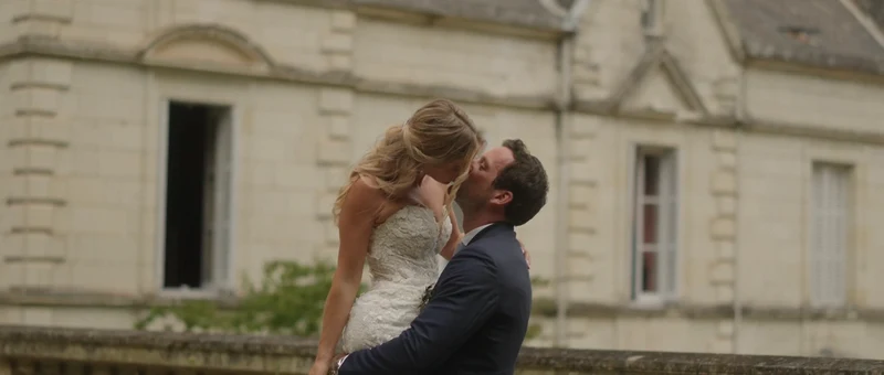 Les mariés s'embrassent devant la façade de pierre du Château de la Barbelinière