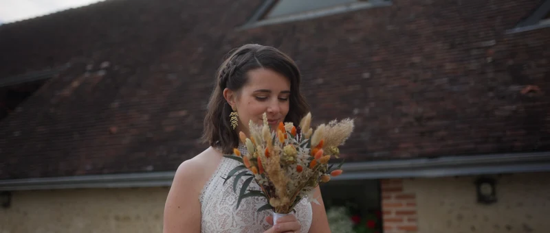 La mariée et son bouquet de fleurs séchées devant le toit de tuiles de La Grange de Fossillon